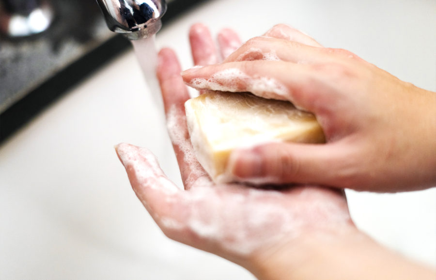 Close-up of hands lathering with a bar of soap under running water at a sink, creating foamy bubbles during handwashing.