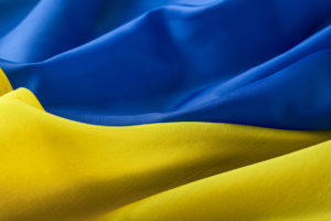 A close-up of fabric in blue and yellow waves, resembling the Ukrainian flag. The upper part is blue, while the lower part is yellow, both with soft folds and smooth textures.