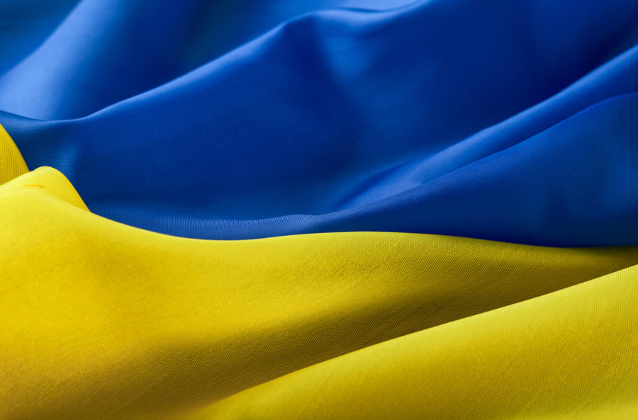 A close-up of fabric in blue and yellow waves, resembling the Ukrainian flag. The upper part is blue, while the lower part is yellow, both with soft folds and smooth textures.