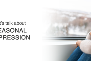 A woman sits by a window, looking outside thoughtfully. The text on the left reads, Lets talk about seasonal depression. Snowy scenery is visible through the window.