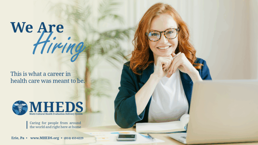Smiling woman with red hair and glasses sits at a desk with a laptop, papers, and a pen, promoting a healthcare hiring ad for MHEDS. Text reads, We are hiring. This is what a career in health care was meant to be.