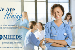 A smiling female nurse stands with arms crossed in a bright hospital room; other healthcare professionals are talking in the background. Text reads We are hiring with contact info for MHEDS, a healthcare organization.