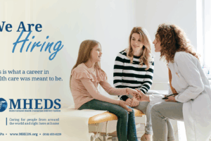 A female doctor smiles while talking to a young girl sitting on an exam table, holding hands with a woman. Text reads We Are Hiring. This is what a career in health care was meant to be. MHEDS logo and contact info are shown.