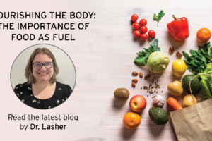 A smiling woman with glasses is pictured next to the text, Nourishing the Body: The Importance of Food as Fuel. Read the latest blog by Dr. Lasher. Fresh fruits and vegetables spill from a paper bag on a light wood surface.
